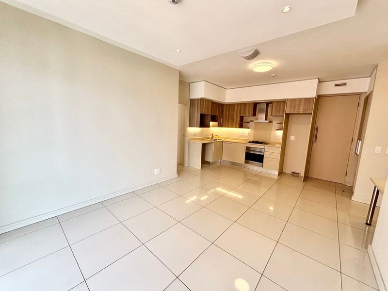 An open-plan living and kitchen area featuring modern built-in cabinetry, integrated appliances, and neutral tiled flooring throughout.