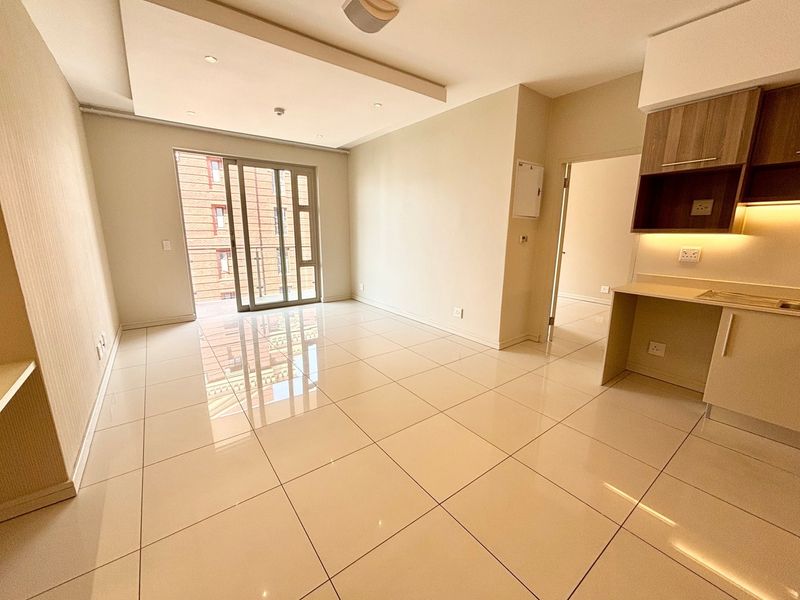 Modern open-plan living area featuring polished porcelain tiles, a sleek drop ceiling with recessed lighting, and a compact, well-lit kitchen with built-in cabinetry.