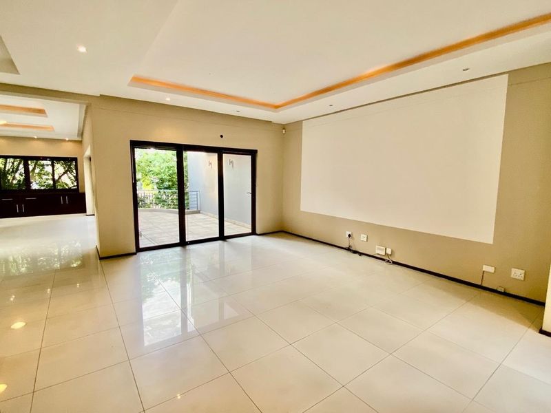 A spacious, empty living area featuring polished tile flooring, recessed ceiling lighting with cove accents, and large sliding glass doors leading to an outdoor patio.