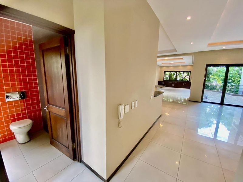 Spacious open-plan living area featuring polished tile floors, recessed lighting, and direct access to an outdoor patio, with an adjacent guest bathroom.
