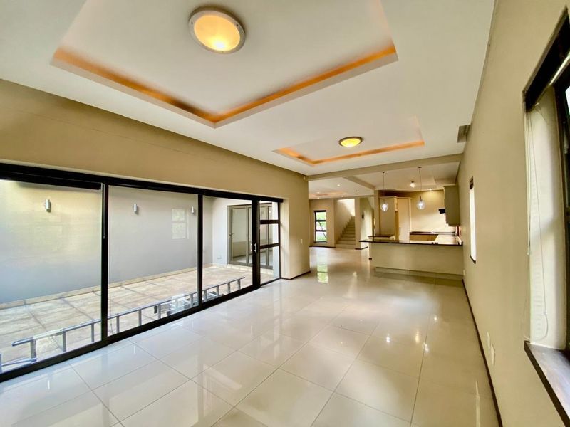 Spacious open-plan living and kitchen area featuring tiled floors, recessed ceiling lighting, and large sliding glass doors leading to an outdoor patio.