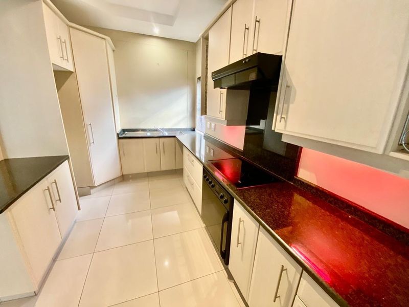 A clean, modern kitchen featuring white cabinetry, dark granite countertops, integrated electric hob, extractor fan, and tiled flooring.
