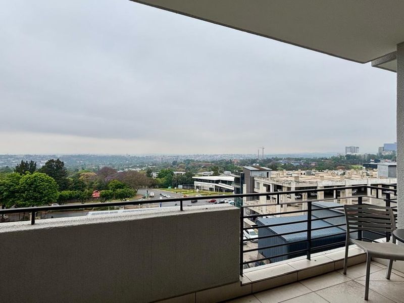 A spacious balcony featuring tiled flooring and metal railings, offering expansive elevated views of the surrounding urban landscape.