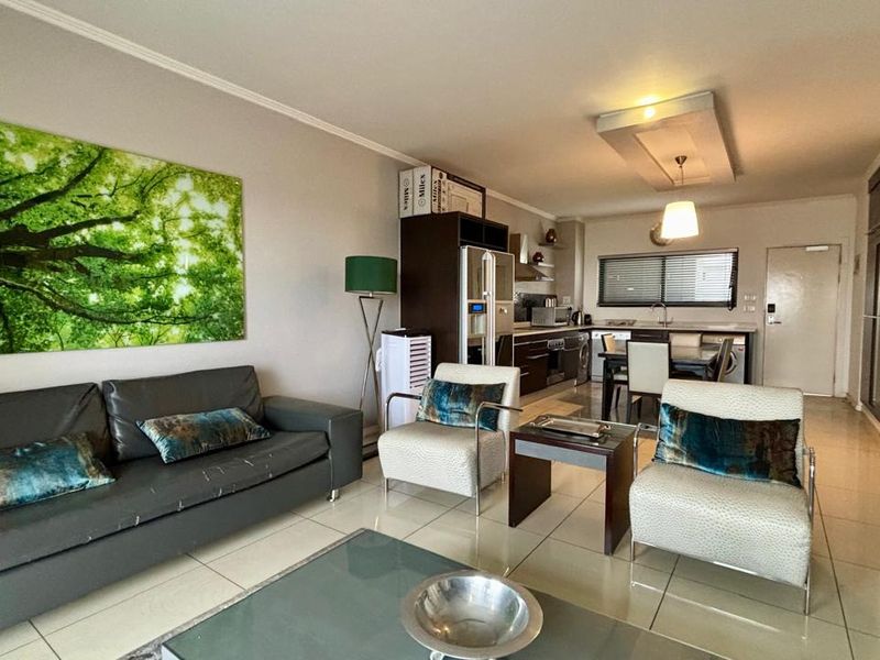 An open-plan living and kitchen area featuring tiled flooring, modern cabinetry, and recessed ceiling lighting, creating a functional and cohesive living space.