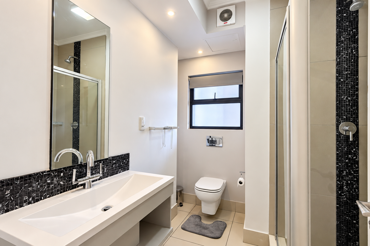 Modern bathroom featuring a wall-mounted toilet, vanity basin with mixer tap, and a glass-enclosed shower with decorative mosaic tile accents.