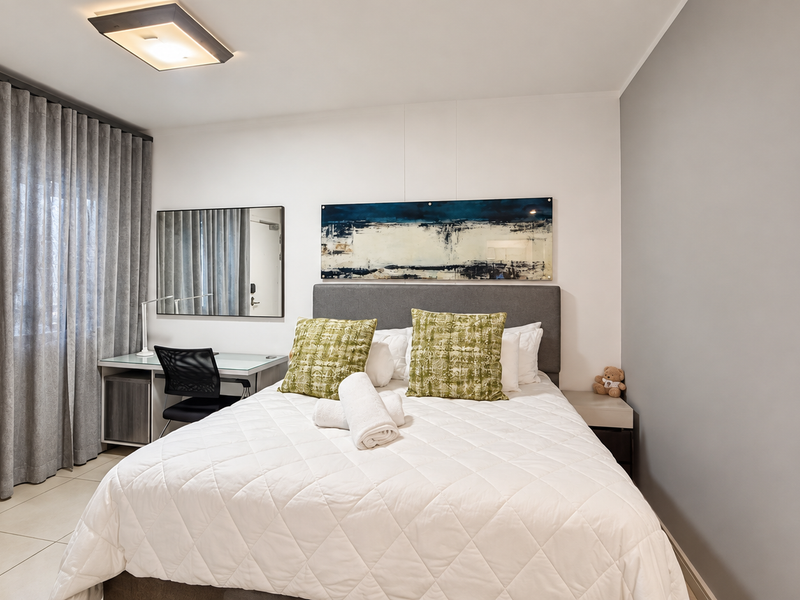 A well-maintained bedroom featuring tiled flooring, a built-in mirror, and neutral wall finishes, providing a clean and comfortable living space.