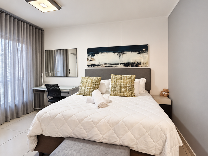 A well-maintained bedroom featuring tiled flooring, neutral walls, and a large window with floor-to-ceiling curtains, creating a bright and comfortable living space.