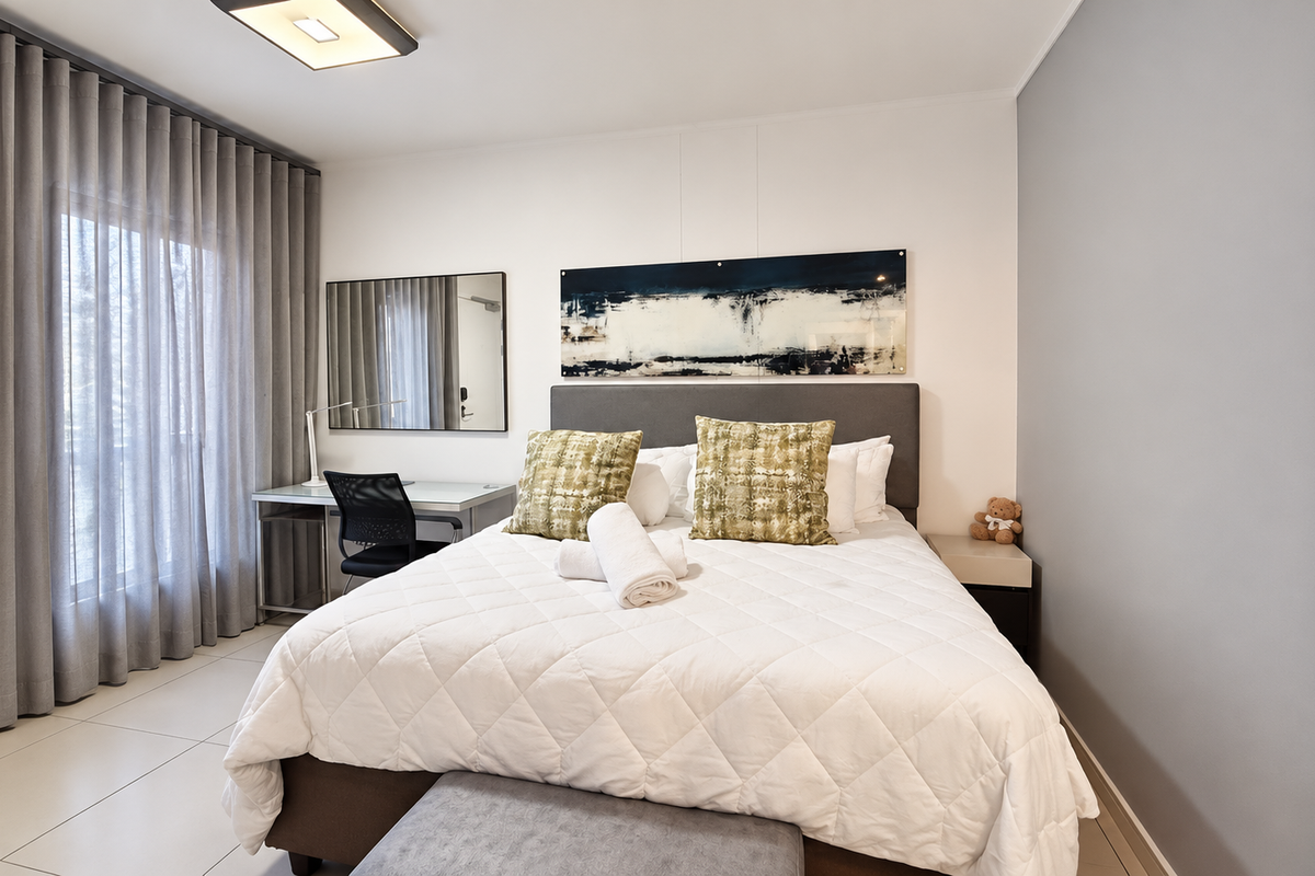 A well-maintained bedroom featuring tiled flooring, neutral walls, and a large window with floor-to-ceiling curtains, creating a bright and comfortable living space.