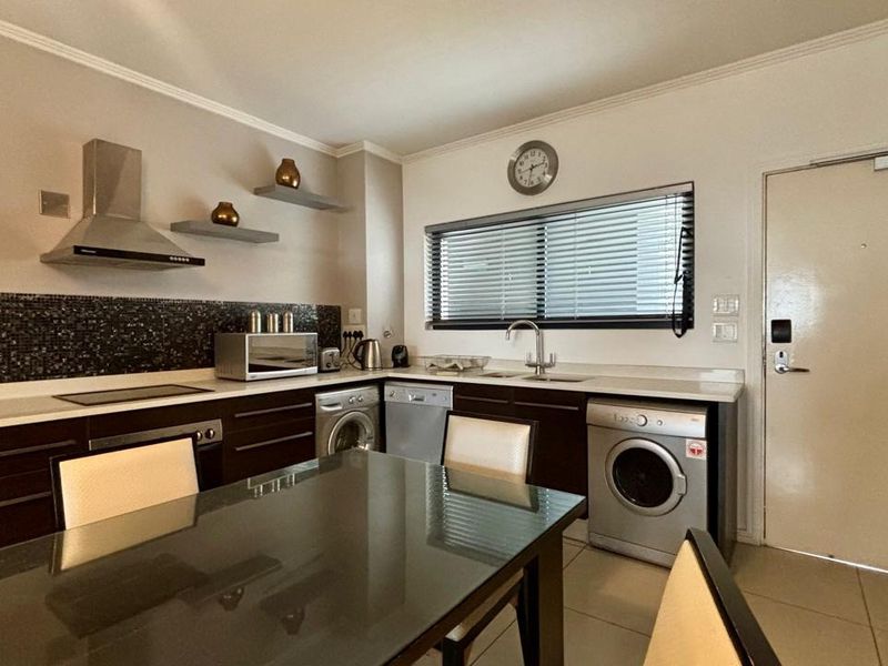 Modern kitchen featuring dark cabinetry, mosaic tile backsplash, stainless steel extractor fan, and integrated appliances with tiled flooring and neutral wall finishes.