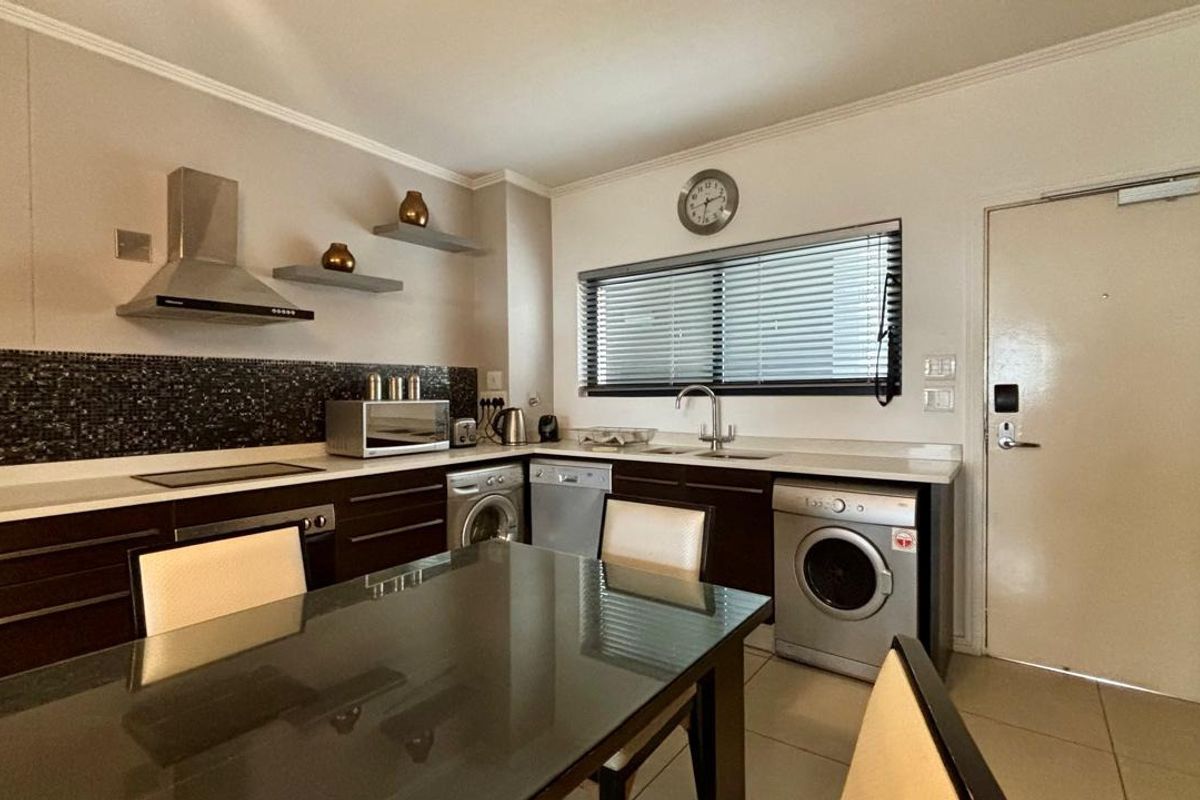 Modern kitchen featuring dark cabinetry, mosaic tile backsplash, stainless steel extractor fan, and integrated appliances with tiled flooring and neutral wall finishes.