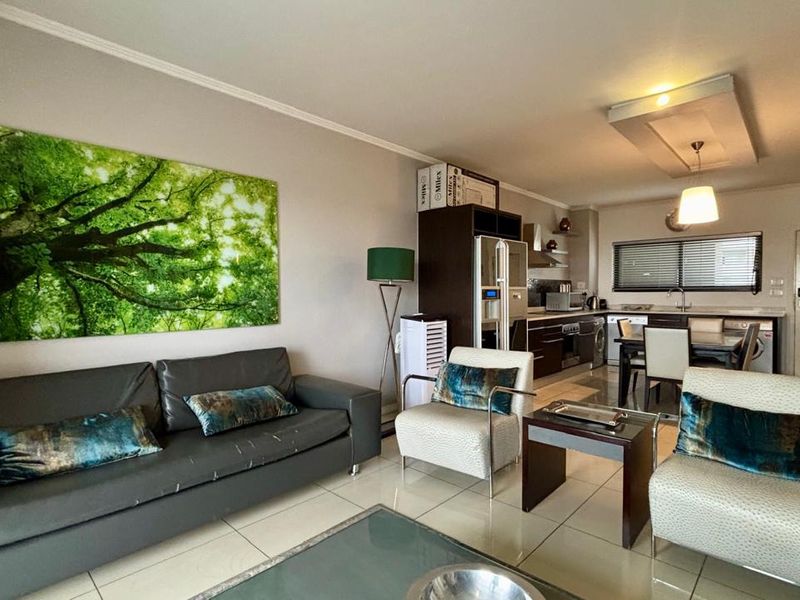 An open-plan living and kitchen area featuring tiled flooring, modern cabinetry, and integrated kitchen appliances, creating a functional and cohesive living space.