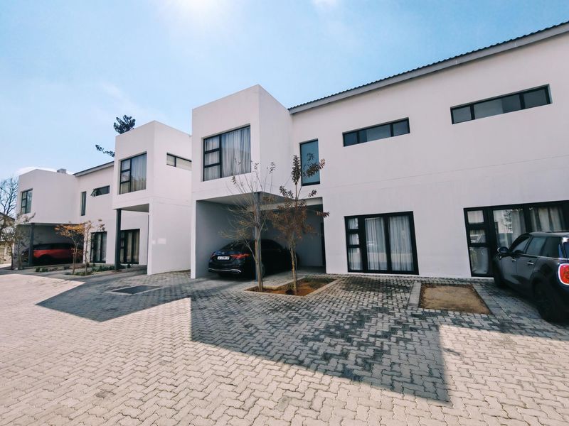 Modern townhouse exterior featuring clean white facades, paved driveway, and covered parking bays with contemporary aluminium window frames.