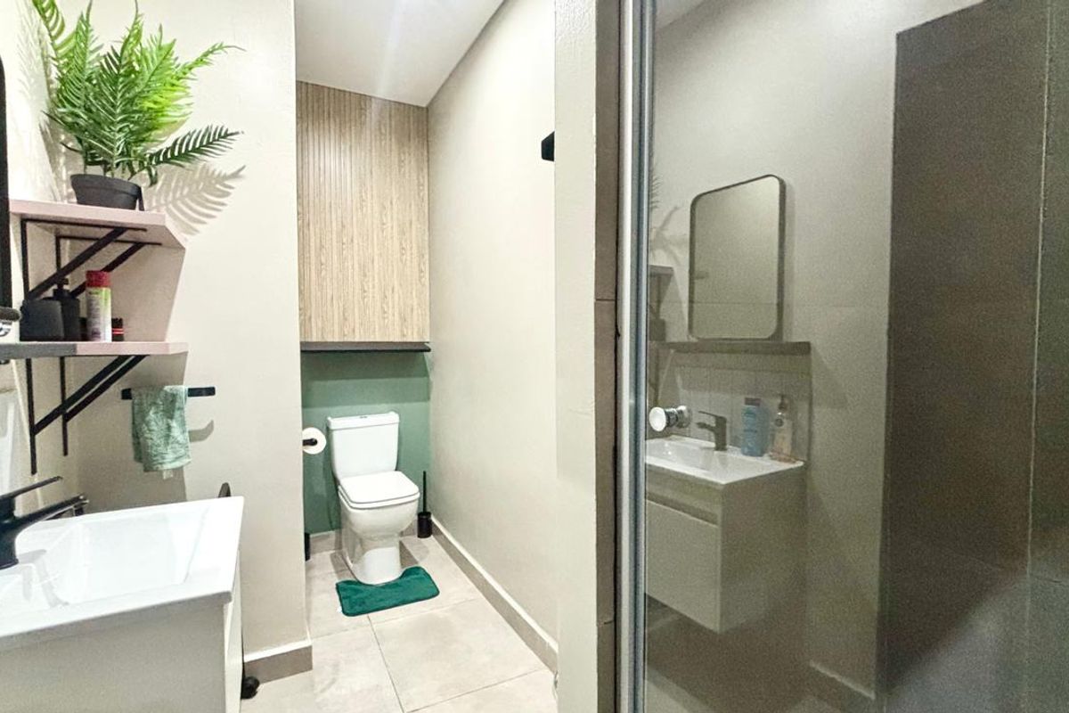 A modern bathroom featuring a vanity with basin, a toilet, and a glass-enclosed shower with neutral tiled flooring and contemporary finishes.
