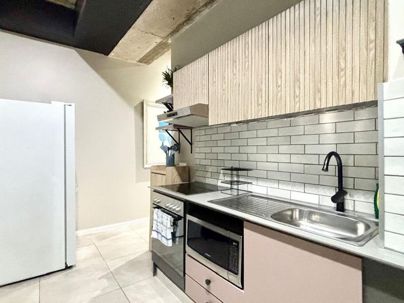 Modern kitchen featuring subway tile backsplash, sleek cabinetry, integrated appliances, and an industrial-style exposed concrete ceiling.