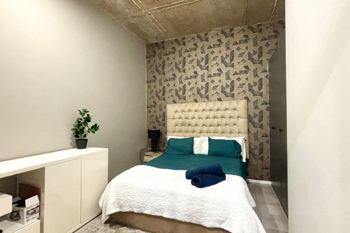 A modern bedroom featuring an exposed concrete ceiling, a stylish patterned feature wall, and integrated built-in wardrobe storage.