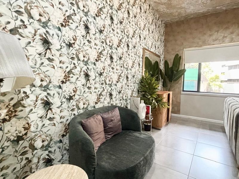 A living room featuring large-format floor tiles, a textured accent wall, and floral wallpaper, providing a distinct aesthetic space.