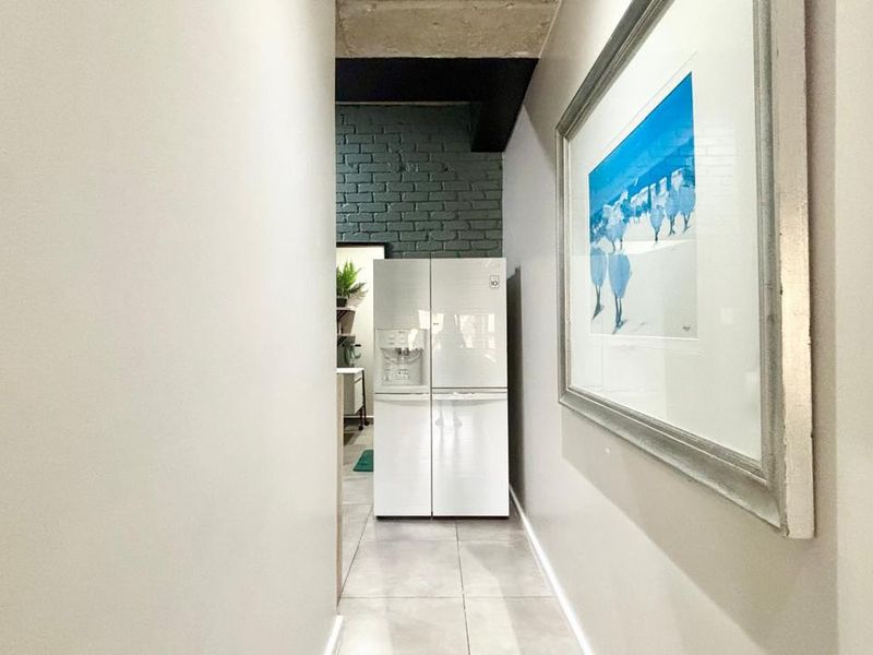 A bright hallway featuring tiled flooring, an exposed concrete ceiling, and a textured painted brick wall leading into the main living area.