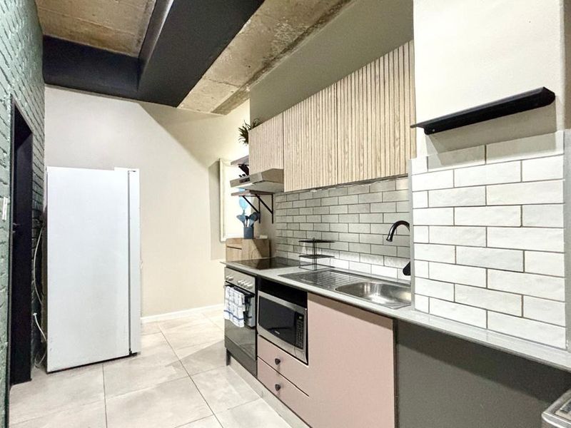 Modern kitchen featuring subway tile backsplash, exposed concrete ceiling, and contemporary cabinetry with integrated oven and stainless steel sink.