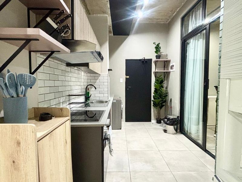 Modern kitchen featuring subway tile backsplash, built-in hob, extractor fan, and exposed concrete ceiling, leading to an outdoor area through a sliding glass door.