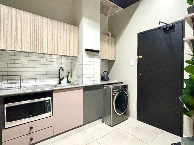Modern kitchen featuring light wood-grain upper cabinets, contrasting lower cabinetry, subway tile backsplash, and integrated laundry space with tiled flooring.