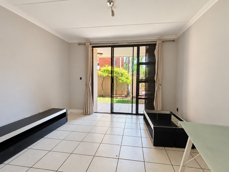 A bright, open-plan living area featuring neutral tiled flooring and a large sliding glass door providing direct access to the outdoor patio and garden.
