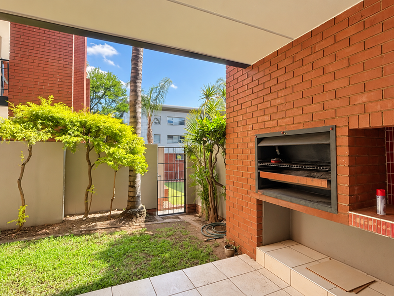 Covered patio area featuring a built-in brick braai with red tiled splashback, overlooking a private garden space.