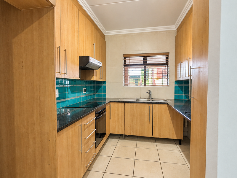 A functional kitchen featuring light wood cabinetry, granite countertops, a tiled backsplash, and integrated appliances including an oven and hob.