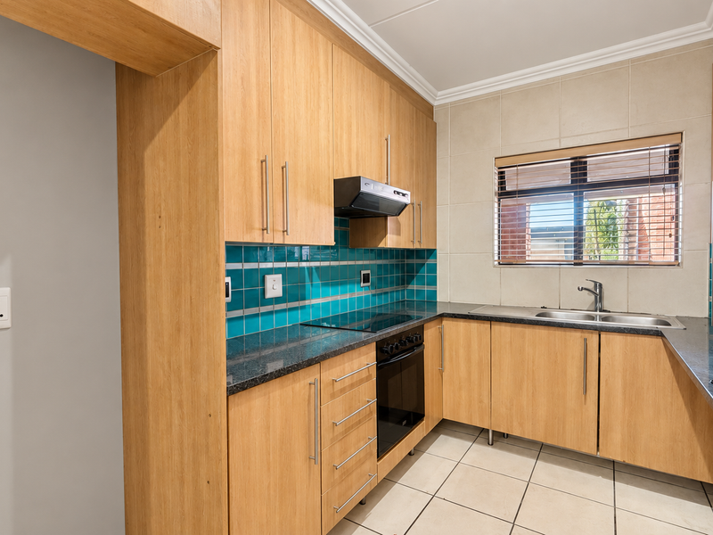 A clean and functional kitchen featuring light wood cabinetry, dark laminate countertops, a built-in oven with hob, and a bright tiled backsplash.