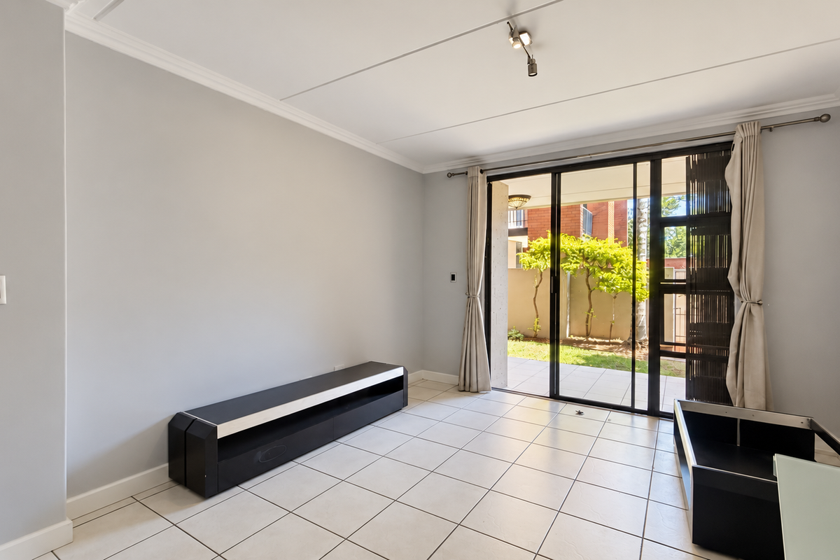 A bright, empty living room featuring neutral tiled flooring, ceiling coving, and large sliding glass doors that open onto a private patio area.