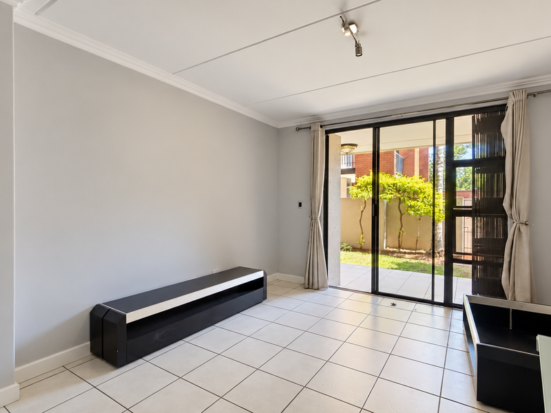 A bright, empty living room featuring neutral tiled flooring, ceiling coving, and large sliding glass doors that open onto a private patio area.