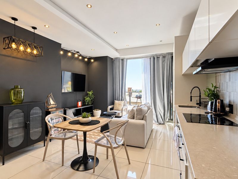 Modern open-plan living area featuring a sleek kitchen with stone countertops, induction hob, and tiled flooring, seamlessly flowing to a bright balcony.