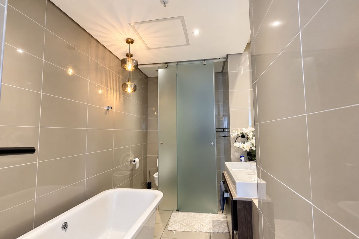 Modern bathroom featuring a sleek freestanding bathtub, wall-mounted vanity, and a contemporary frosted glass sliding door, finished with neutral ceramic wall tiles.