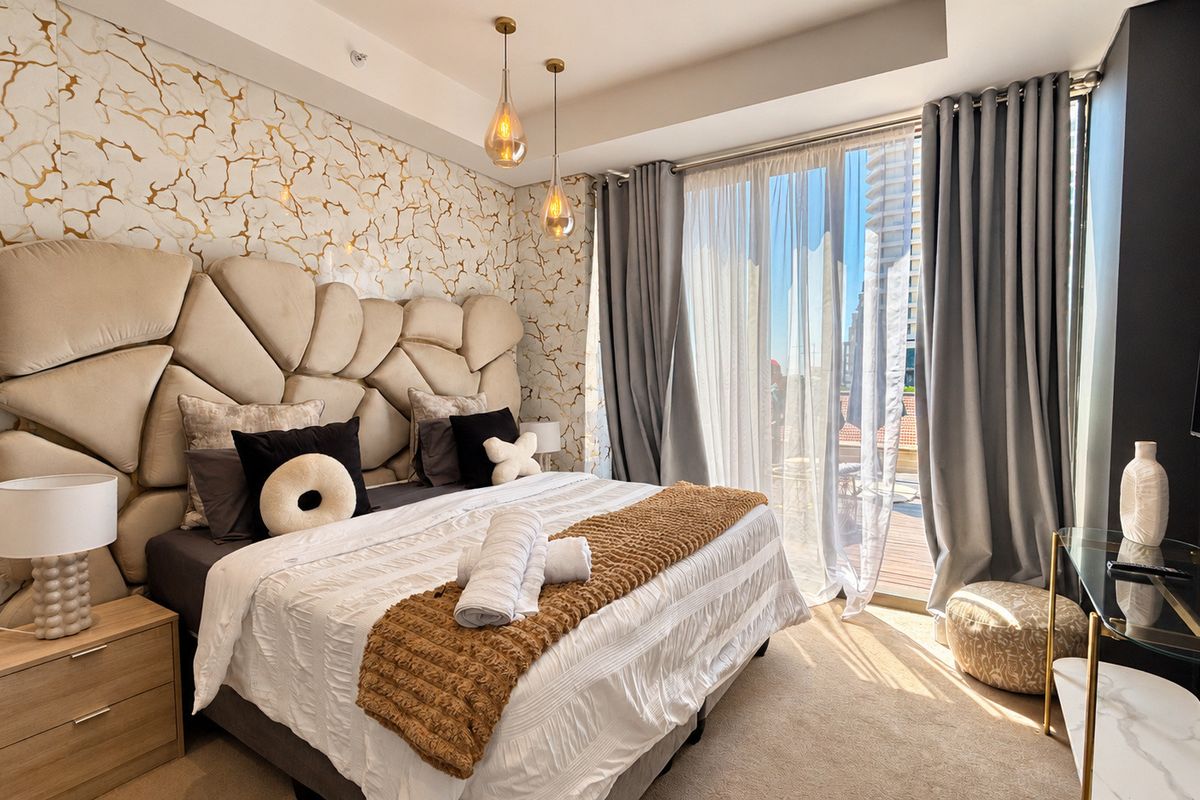 A well-appointed bedroom featuring decorative patterned wallpaper, modern pendant lighting, and floor-to-ceiling curtains leading to an outdoor balcony area.