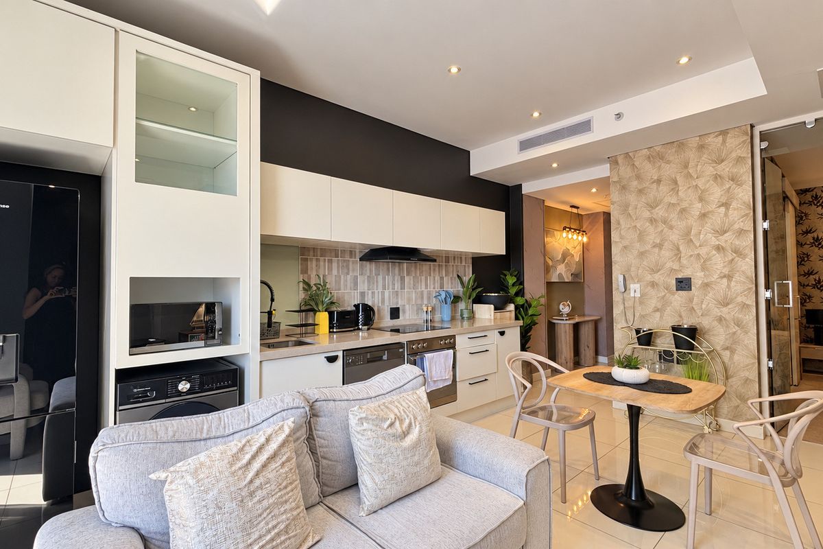 Modern open-plan kitchen and living area featuring sleek cabinetry, integrated appliances, tiled flooring, and a stylish wallpaper accent wall.