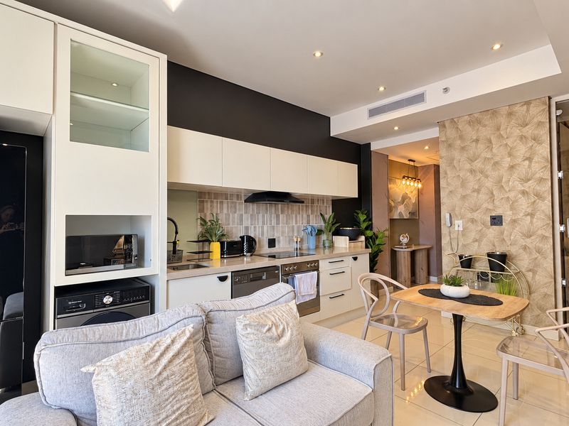 Modern open-plan kitchen and living area featuring sleek cabinetry, integrated appliances, tiled flooring, and a stylish wallpaper accent wall.