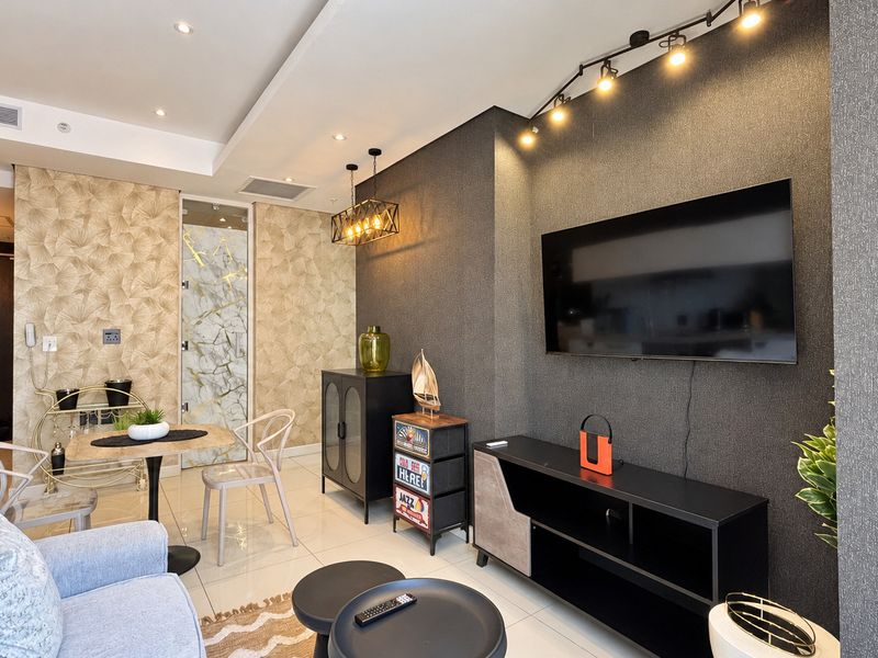 Modern living room featuring textured feature walls, recessed downlighting, track lighting, and polished tiled flooring in an open-plan apartment layout.