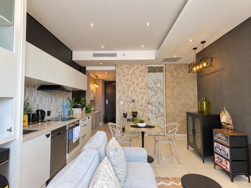 Modern open-plan living area featuring a sleek kitchen with integrated appliances, recessed lighting, and high-quality tiled flooring throughout.