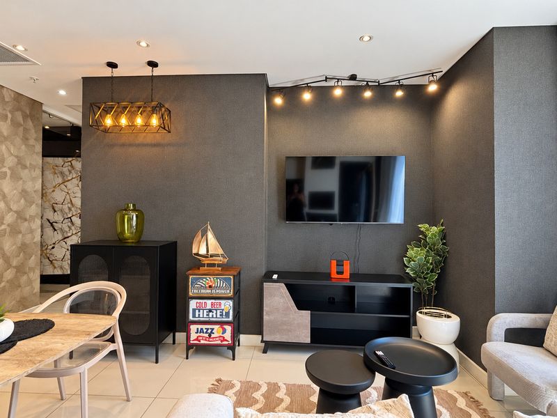 A modern open-plan living and dining area featuring textured feature walls, contemporary track lighting, recessed ceiling lights, and sleek tiled flooring.