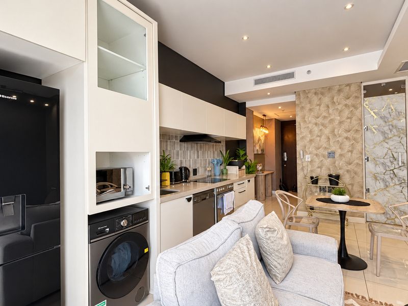 Modern open-plan apartment featuring a sleek kitchen with built-in appliances, tiled backsplash, and recessed lighting, seamlessly flowing into the living and dining area.