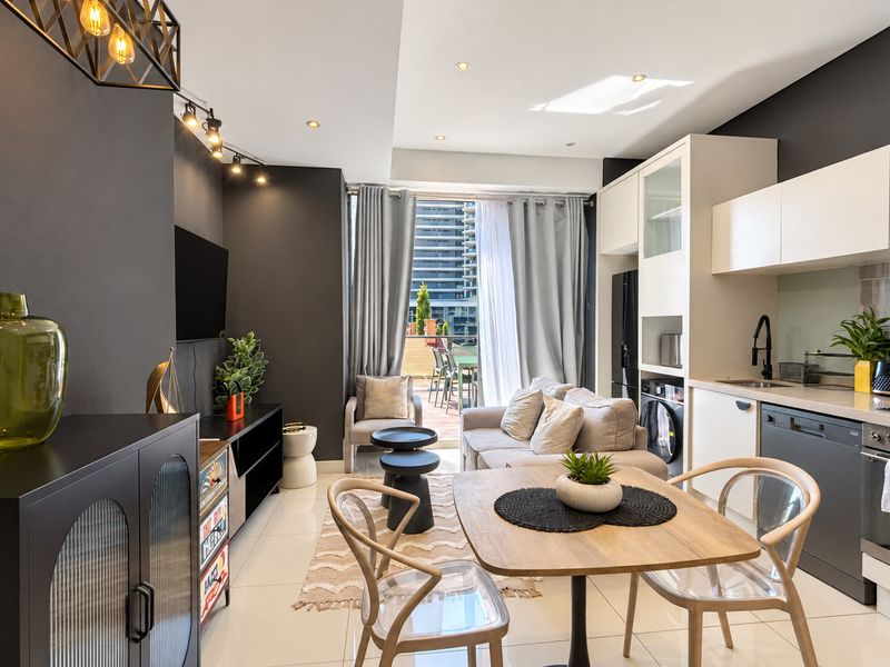 Modern open-plan living area featuring a sleek kitchen with integrated appliances, tiled flooring, and direct access to a private balcony.