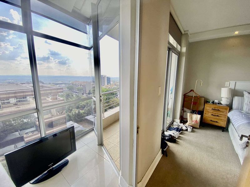 A bedroom featuring floor-to-ceiling windows and a sliding glass door leading to a private balcony with expansive city views.