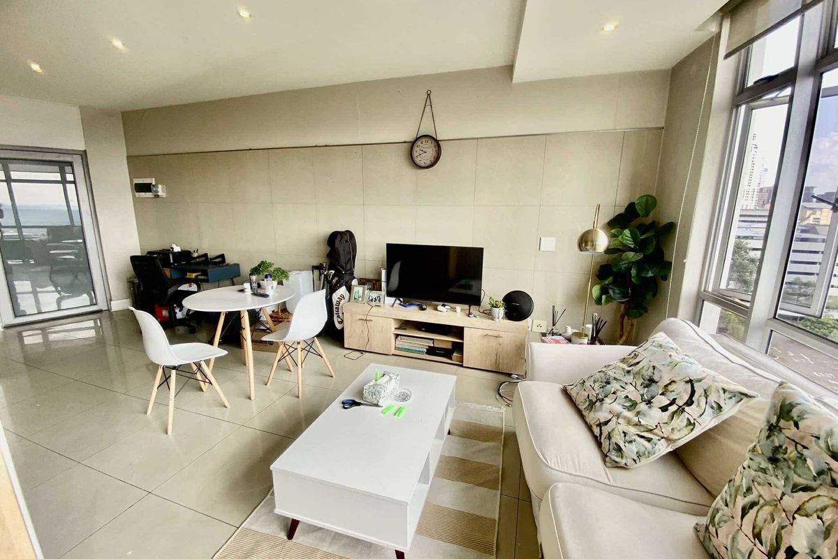 A bright and modern living room featuring large floor-to-ceiling windows, neutral tiled flooring, and contemporary stone-look wall cladding with recessed lighting.