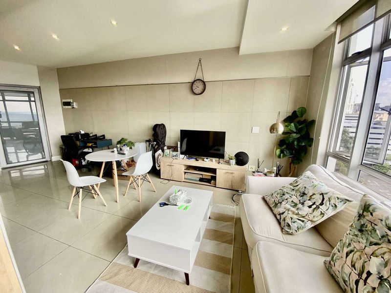 A bright and modern living room featuring large floor-to-ceiling windows, neutral tiled flooring, and contemporary stone-look wall cladding with recessed lighting.