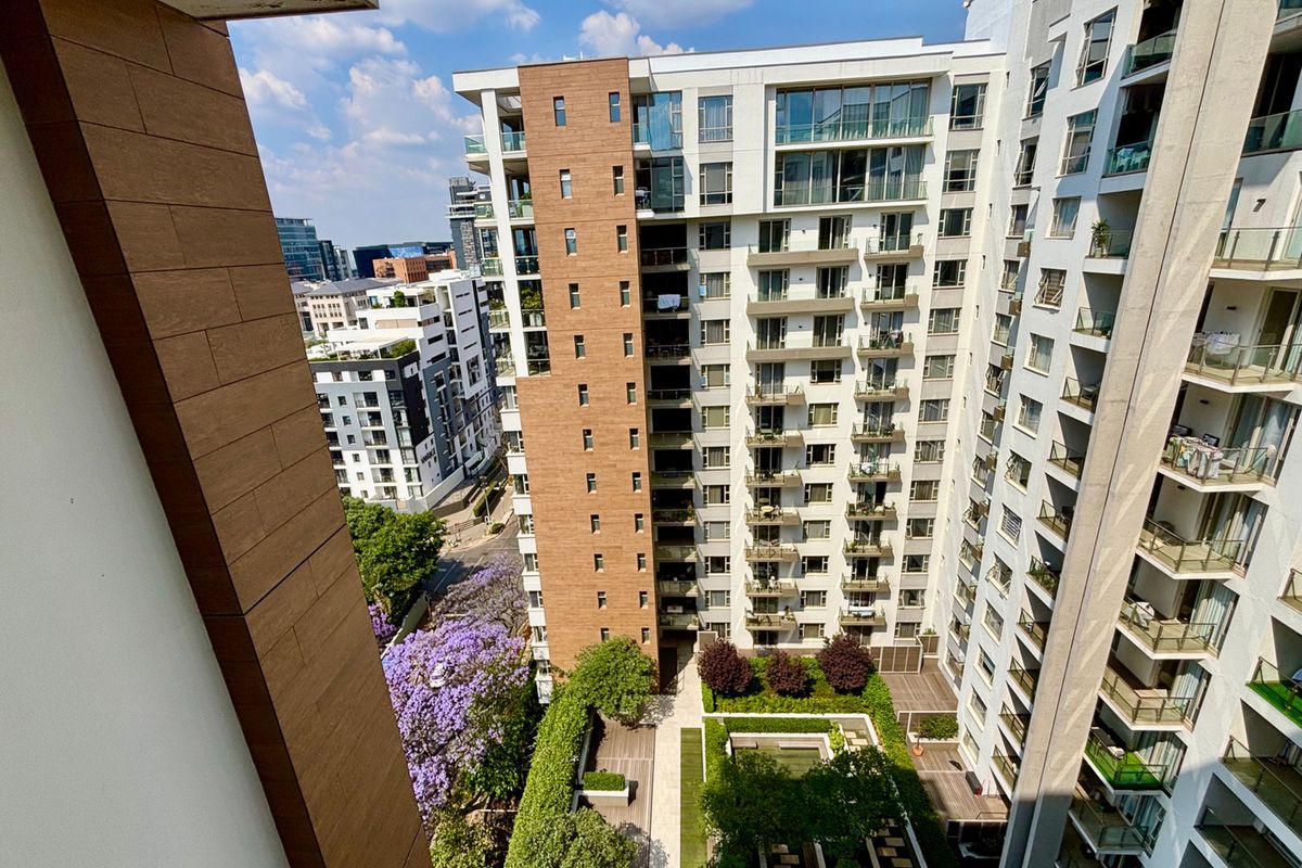 An elevated aerial view of a modern apartment complex featuring multiple balconies, landscaped courtyard areas, and contemporary building facade finishes.