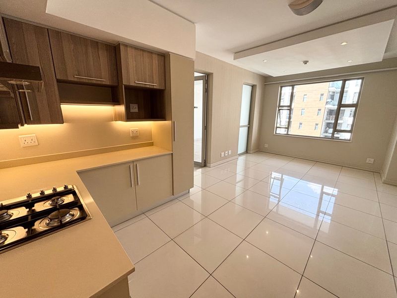Modern open-plan kitchen and living area featuring sleek cabinetry, stone countertops, gas hob, and polished tiled flooring with abundant natural light.