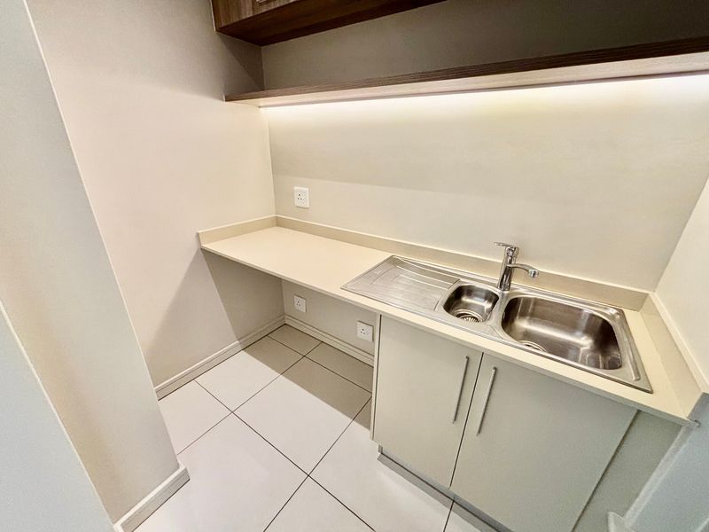 A clean and modern scullery area featuring a stainless steel double sink, stone countertop, under-counter cabinetry, and integrated LED shelf lighting.