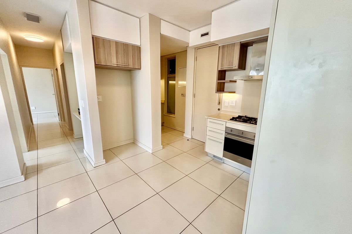 A clean, modern kitchen featuring built-in cabinetry, a gas hob, an oven, and an extractor fan, complemented by neutral tiled flooring throughout.