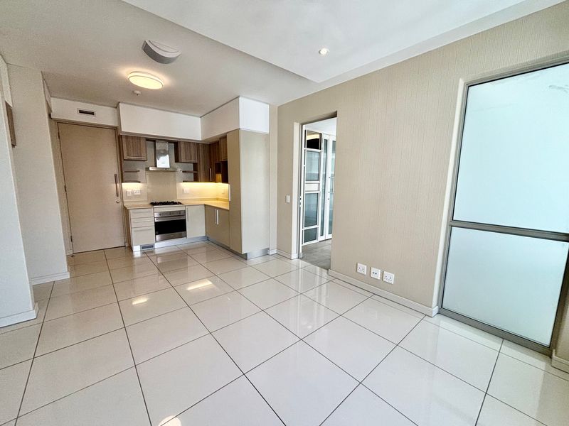 Modern open-plan living area featuring sleek tiled floors, recessed lighting, and a compact, well-equipped kitchen with built-in cabinetry and integrated appliances.