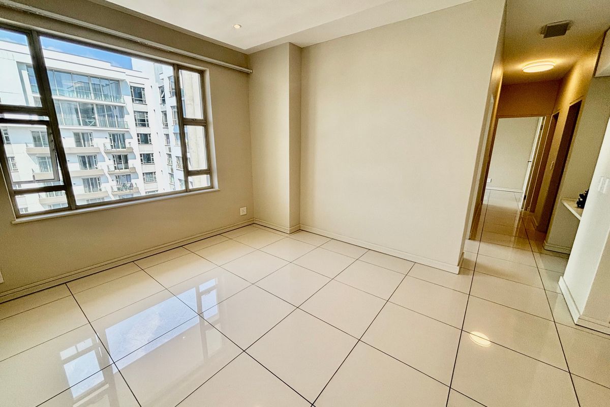 A bright and spacious empty living area featuring neutral tiled flooring, recessed lighting, and a large window providing natural light.