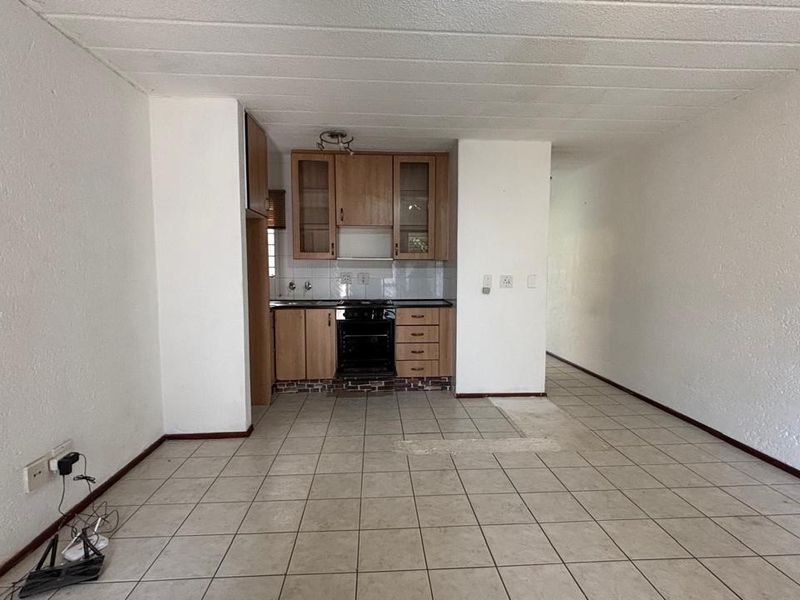An open-plan living and kitchen area featuring tiled flooring, built-in wooden cabinetry, and an integrated oven, presenting a blank canvas for renovation.